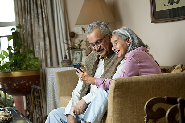 Äldre par sitter i soffan och tittar på smartphone